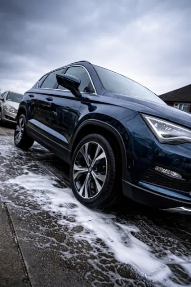 Dark SUV covered in snow foam during the pre-wash stage of an exterior detail