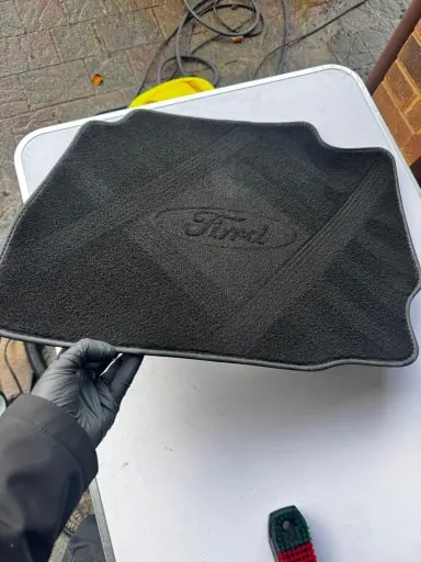 A Ford floor mat held up after deep cleaning, showing restored texture and colour