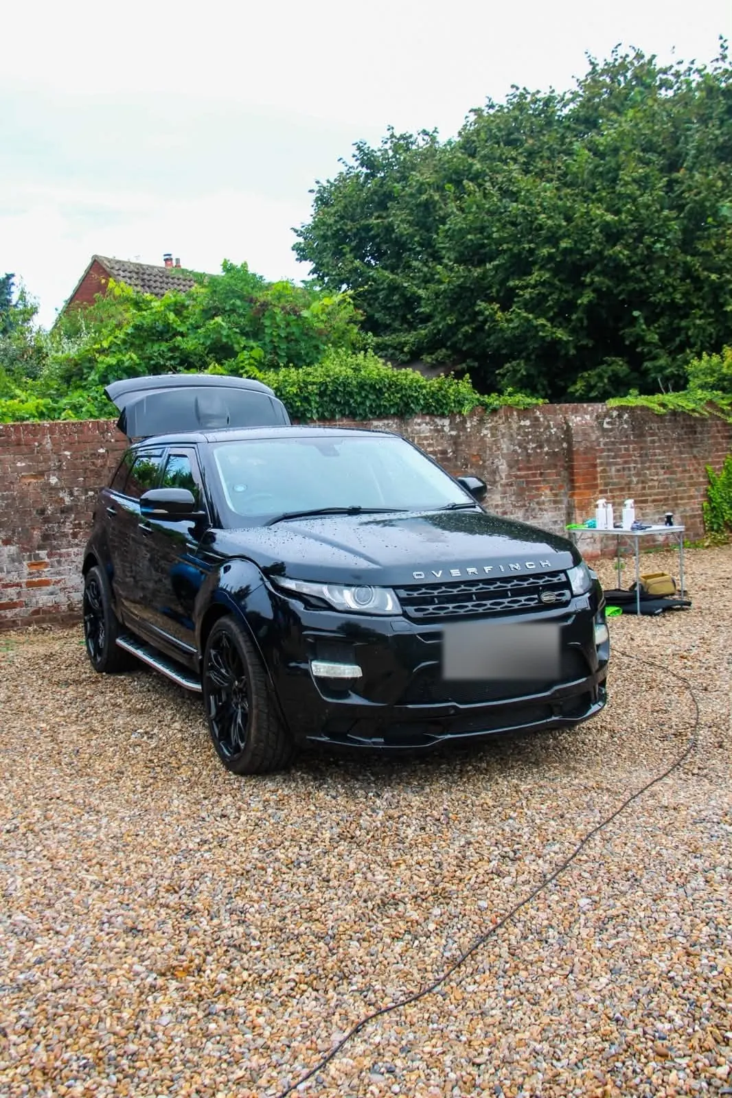 Black Overfinch Range Rover Evoque on a gravel driveway after a full exterior detail, water still beading on the paint