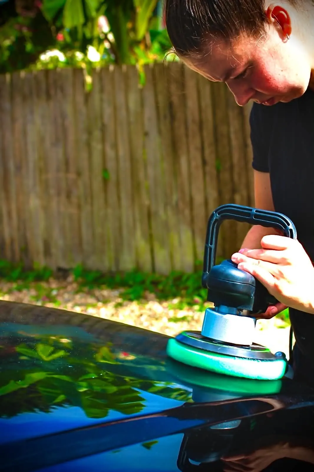 Dual action machine polisher with a blue pad working across the bonnet of a black car