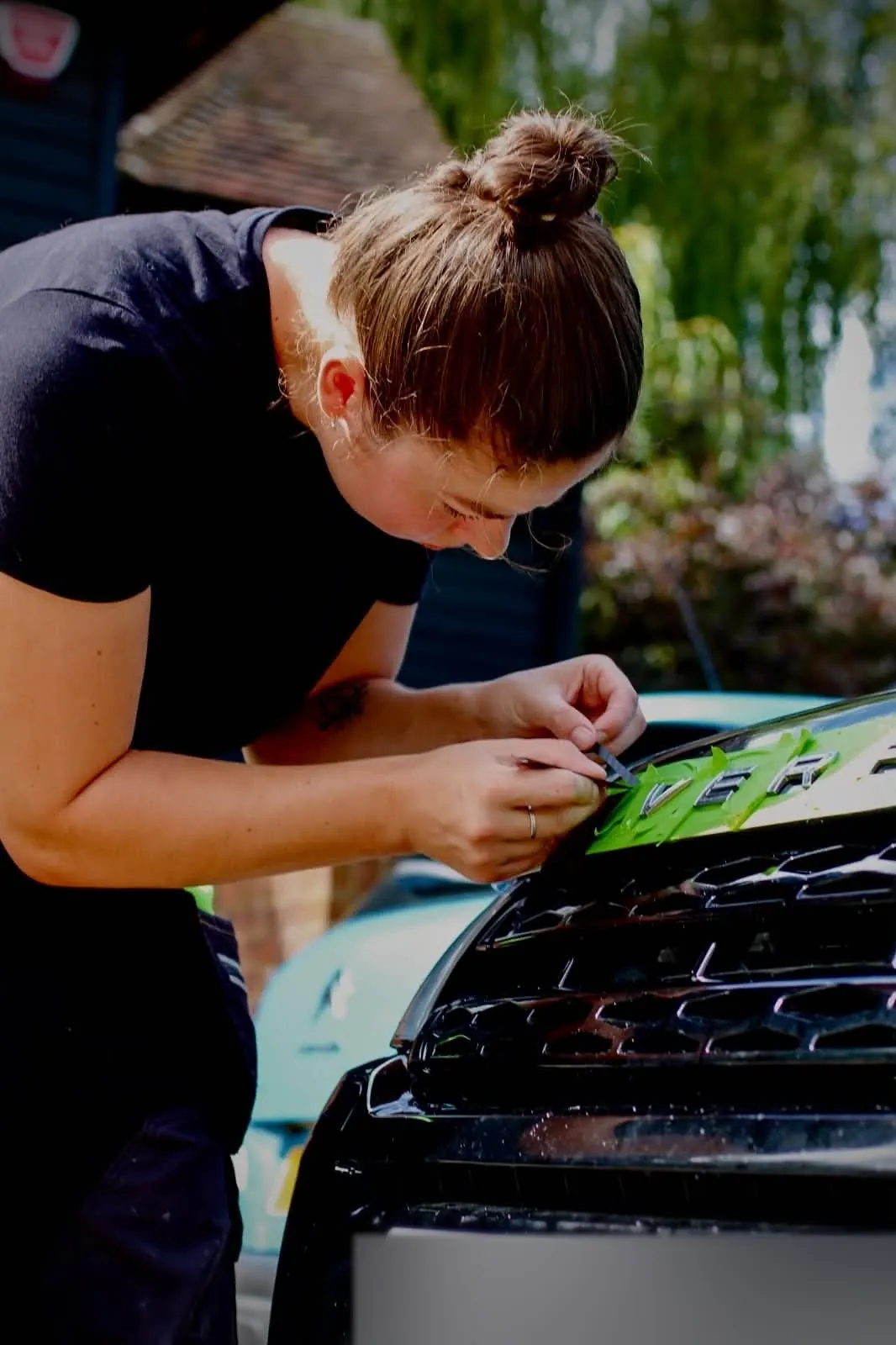 Lettering being lifted from a car bonnet with the surrounding paint masked off in green tape