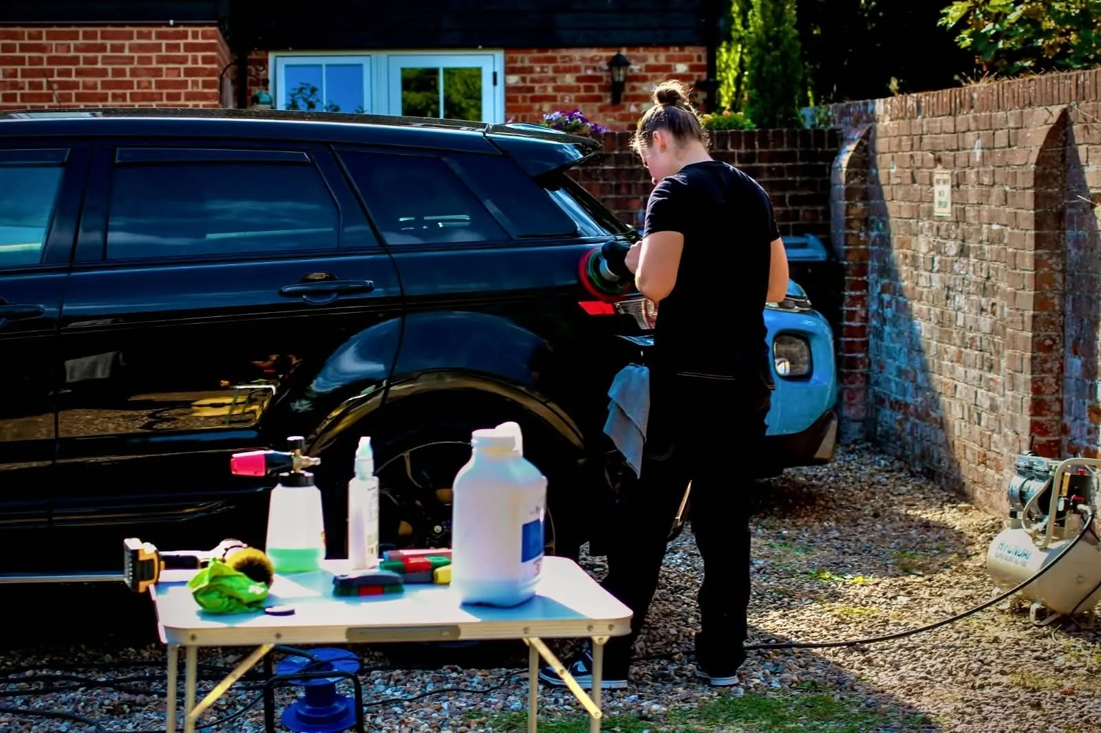 Ash detailing a black Range Rover Evoque on a customer's driveway with her equipment laid out beside the car