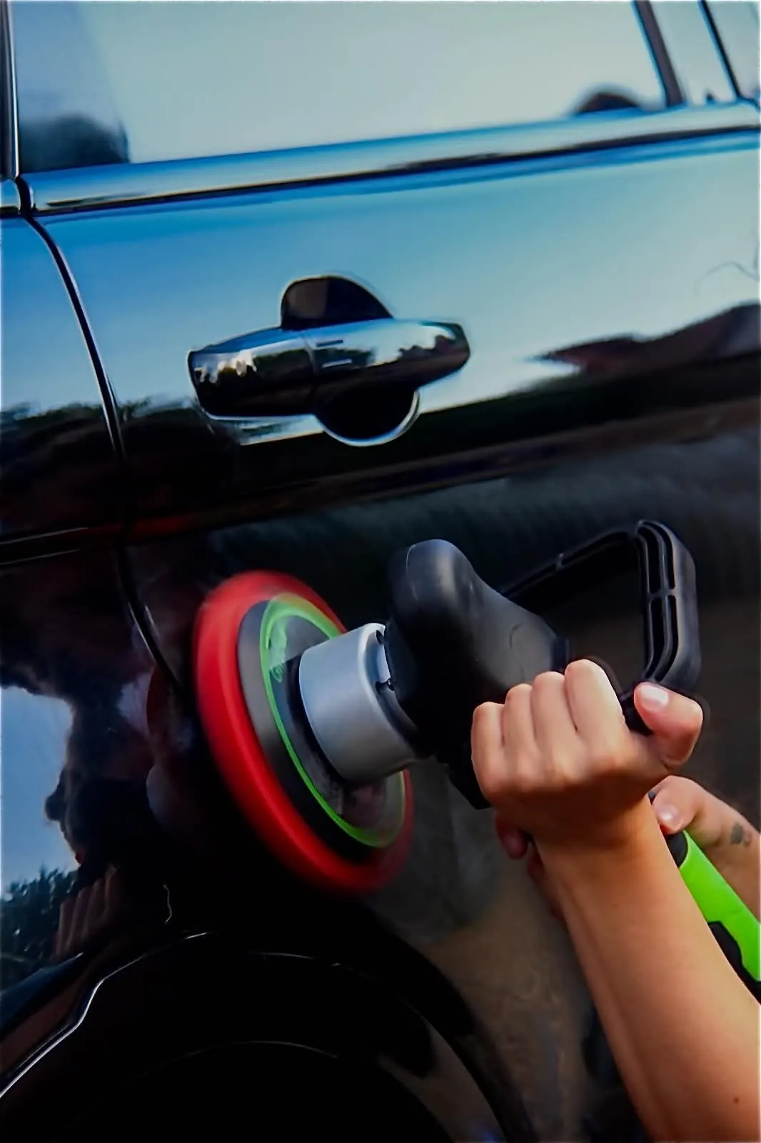 Machine polisher working the paint beside the door handle of a black car