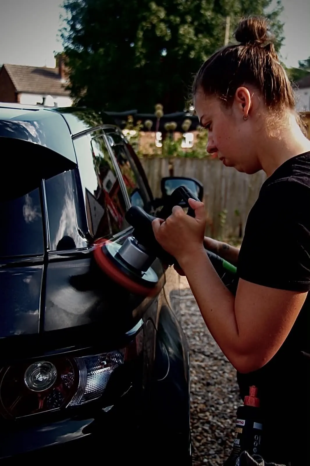 Machine polishing the front wing of a black car beside the headlight